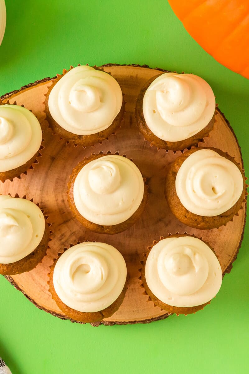 overhead image of pumpkin cupcakes topped with cream cheese frosting on a wood slice serving tray