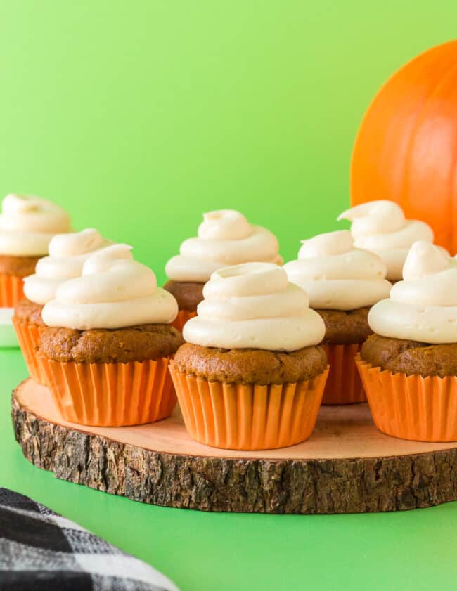 pumpkin cupcakes topped with cream cheese frosting on a wood slice serving tray