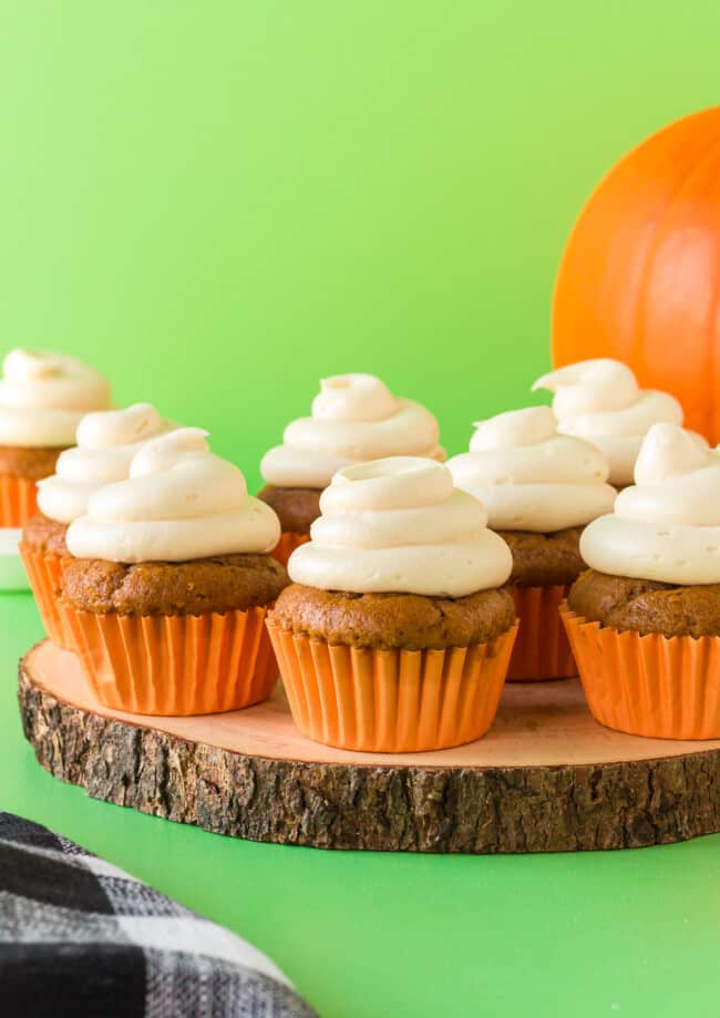 pumpkin cupcakes topped with cream cheese frosting on a wood slice serving tray