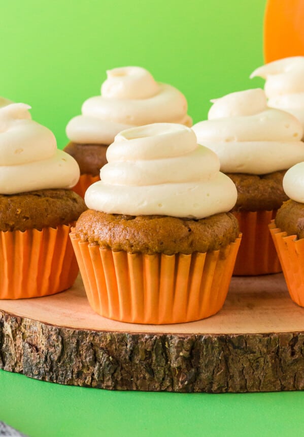 pumpkin cupcakes topped with cream cheese frosting on a wood slice serving tray