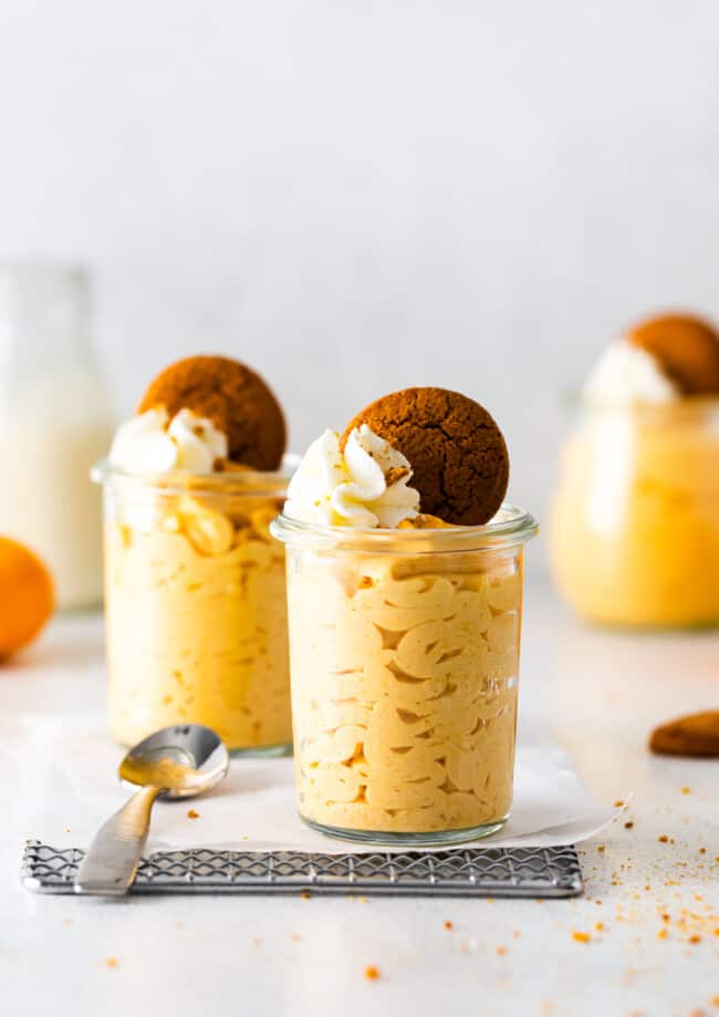 2 glass jars of pumpkin mousse topped with whipped cream and gingersnap cookies