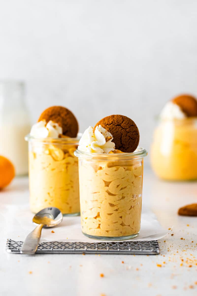 2 glass jars of pumpkin mousse topped with whipped cream and gingersnap cookies