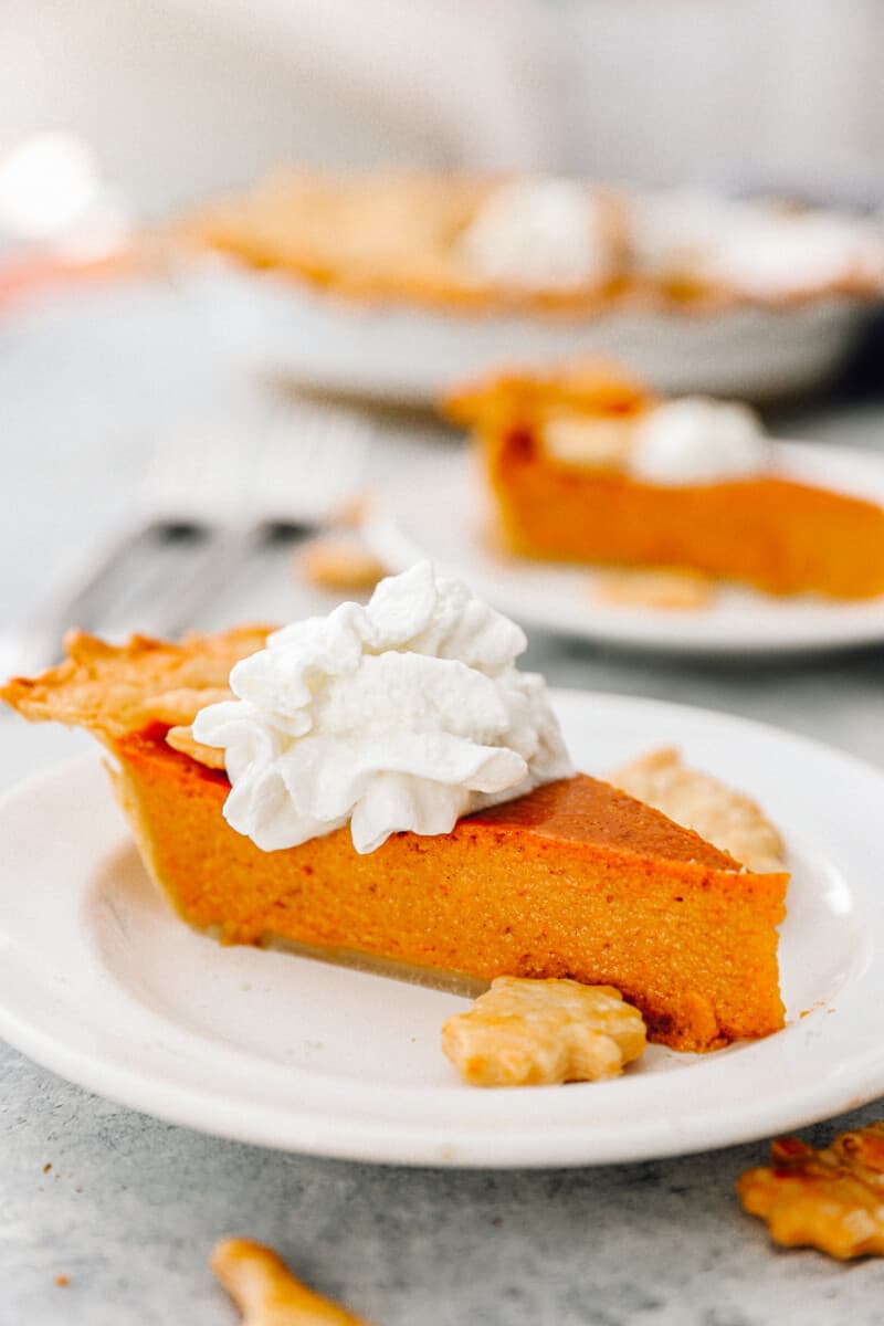 slice of pumpkin pie topped with whipped cream on a white plate