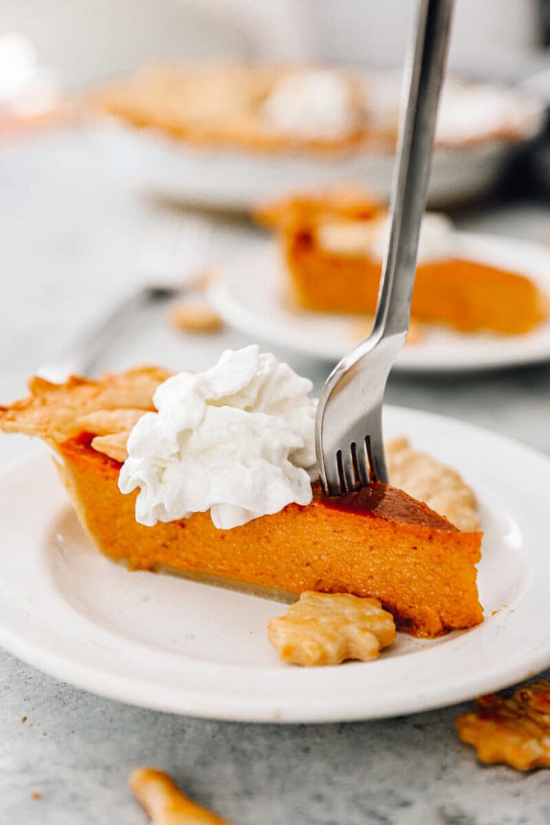 slice of pumpkin pie topped with whipped cream on a white plate with a fork