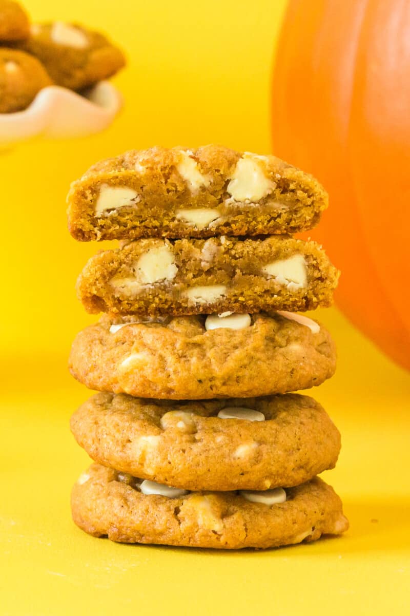 stack of 5 pumpkin pudding cookies with white chocolate chips with one cookie broken in half showing the inside texture
