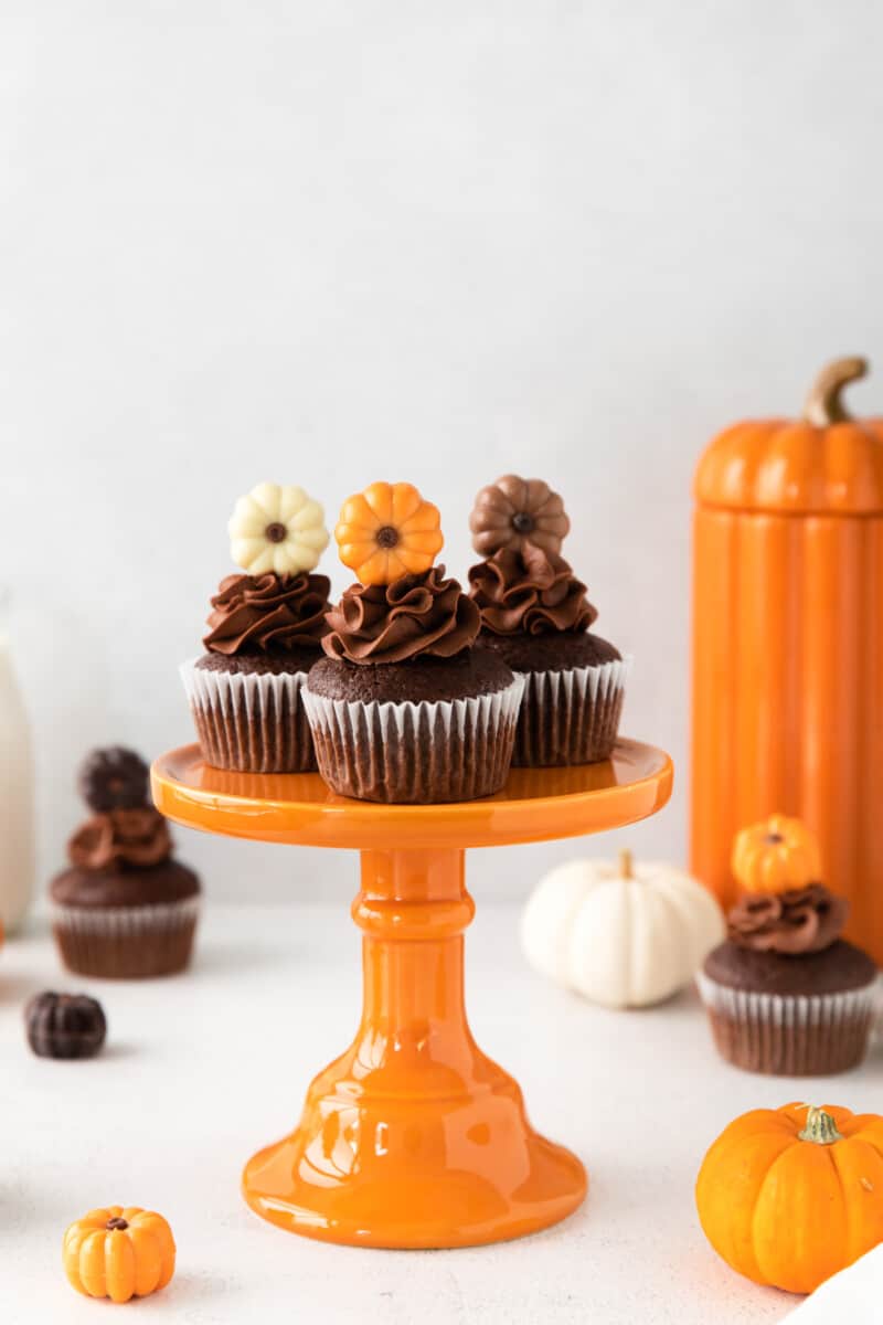 3 chocolate pumpkin cupcakes on an orange cake stand.
