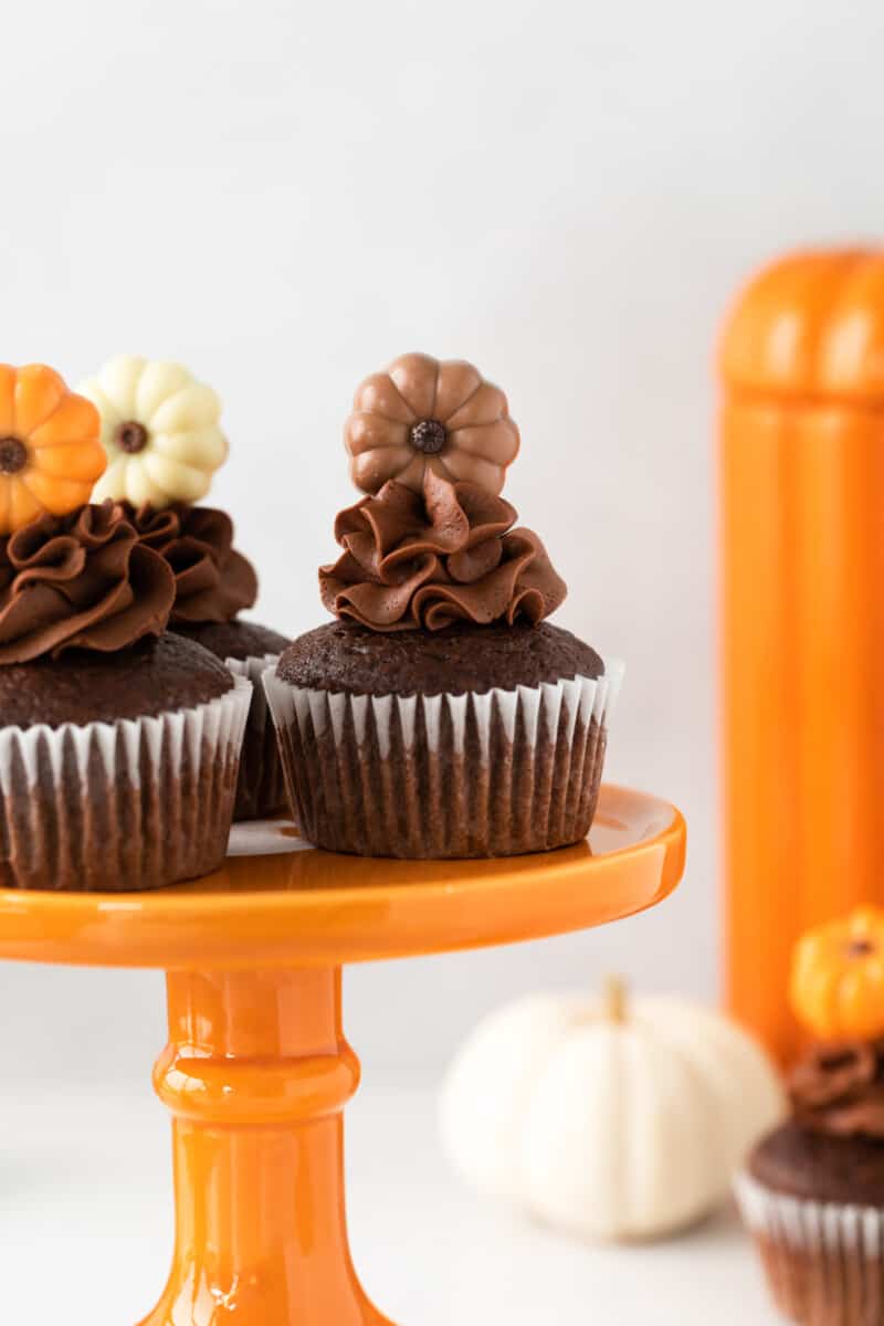 close up of 3 chocolate pumpkin cupcakes on an orange cake stand.