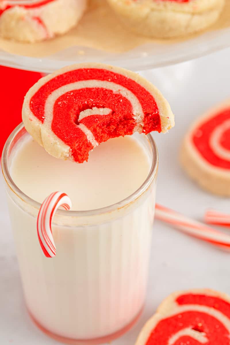 white and red pinwheel cookie on top of a glass of milk