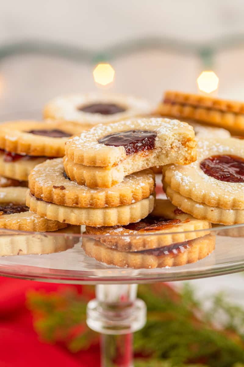linzer cookies on a glass cake stand with a bite taken from one
