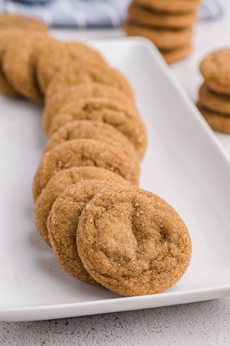 stacked ginger molasses cookies snaking on a white rectangular plate.