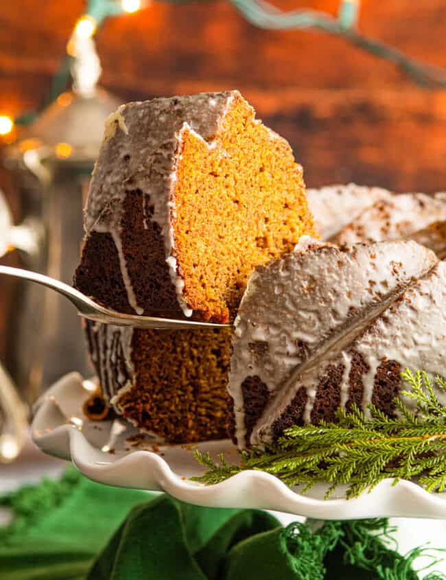 slice of gingerbread bundt cake removed from a bundt cake on a white cake stand with a cake server.