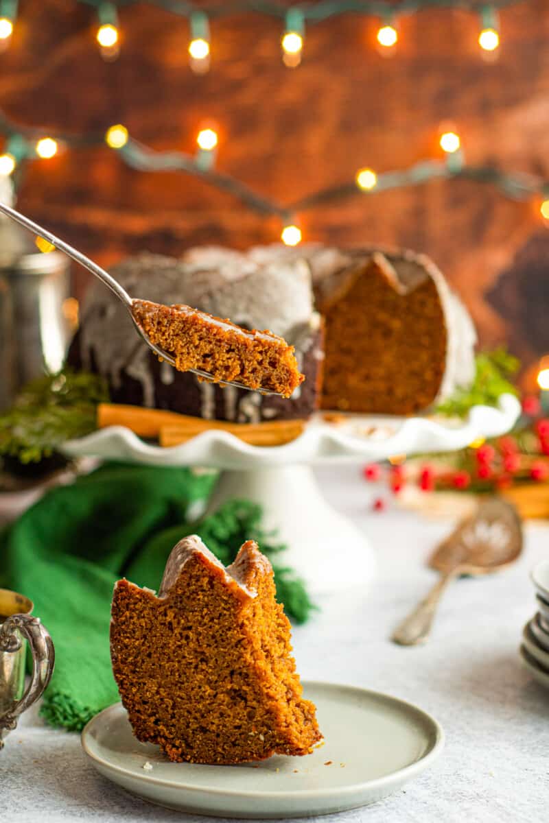 forkful of gingerbread bundt cake hovering above a slice on a white plate.