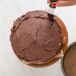 hand spreading frosting onto a chocolate cake