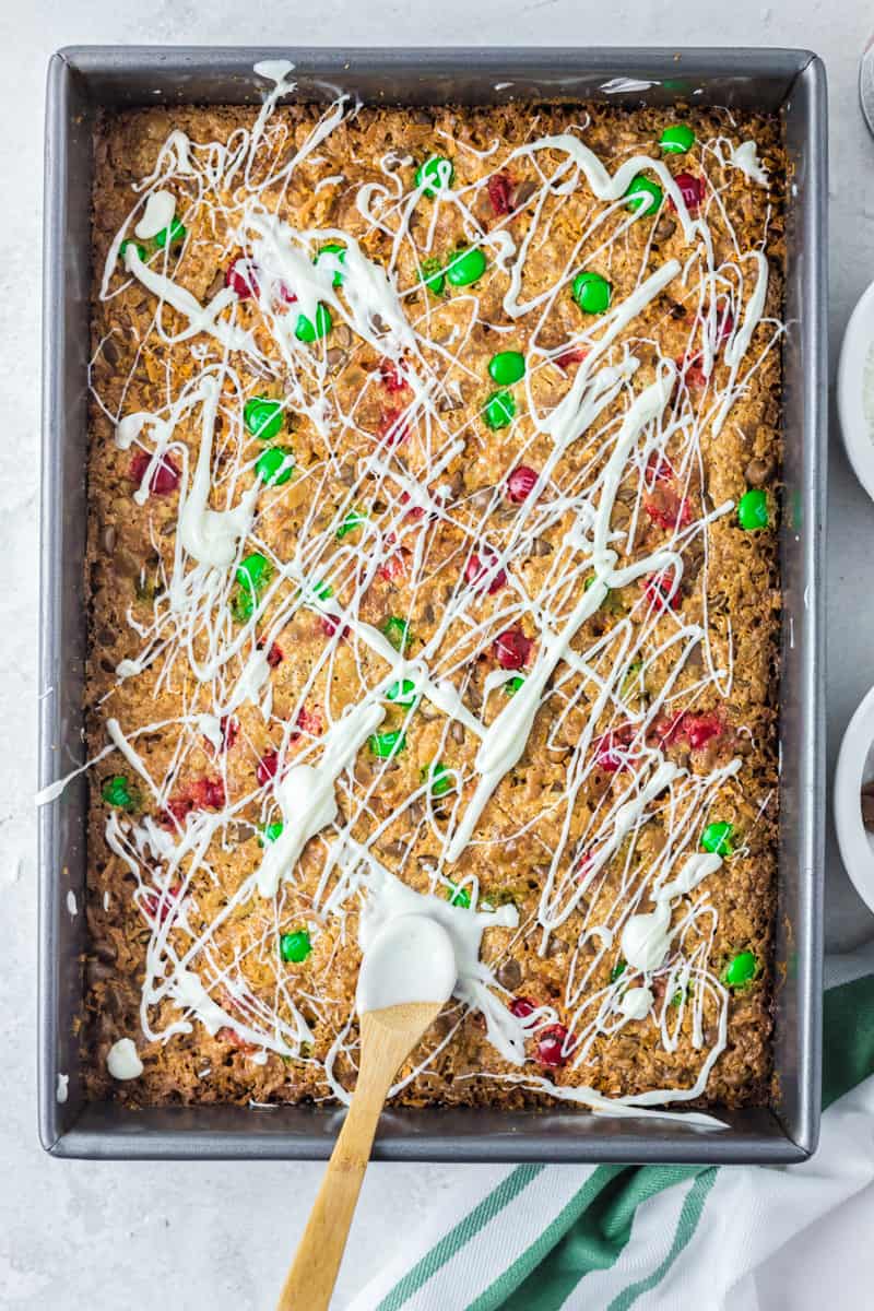 drizzling white chocolate onto magic cookie bars in a baking pan
