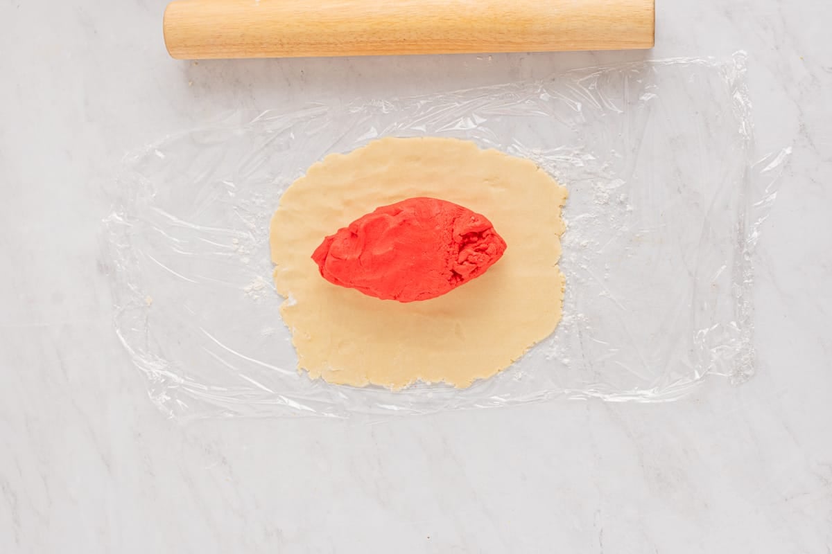 white cookie dough rolled out onto plastic wrap with red cookie dough on top