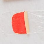 rolling red and white pinwheel cookie dough on plastic wrap