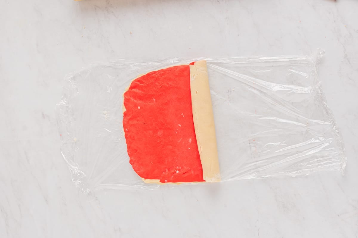 rolling red and white pinwheel cookie dough on plastic wrap