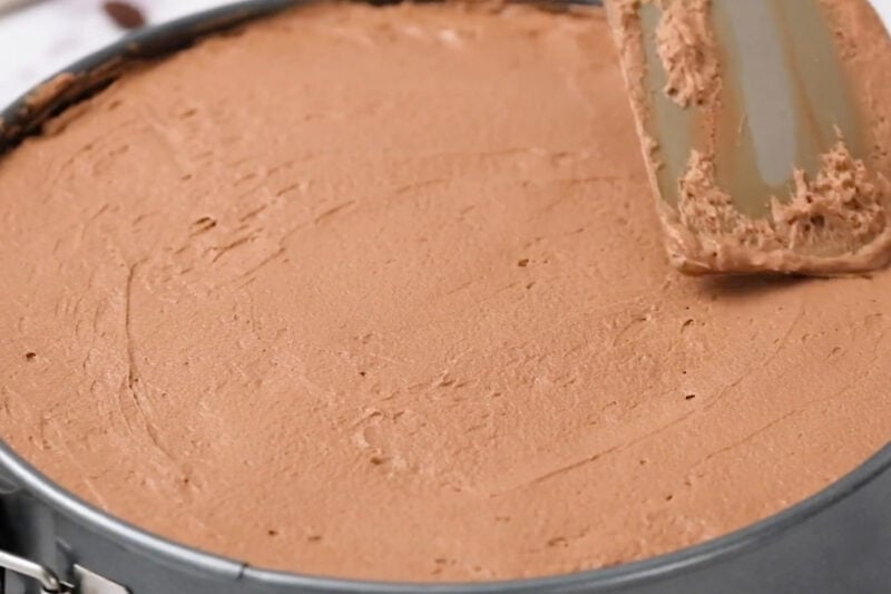 spreading chocolate mousse over chocolate cake in a springform pan.