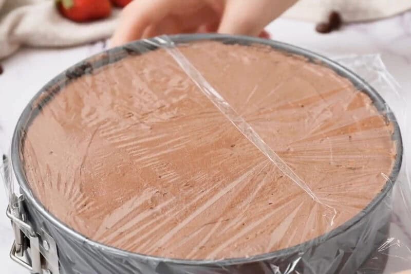 chocolate mousse cake covered with plastic wrap in a springform pan.