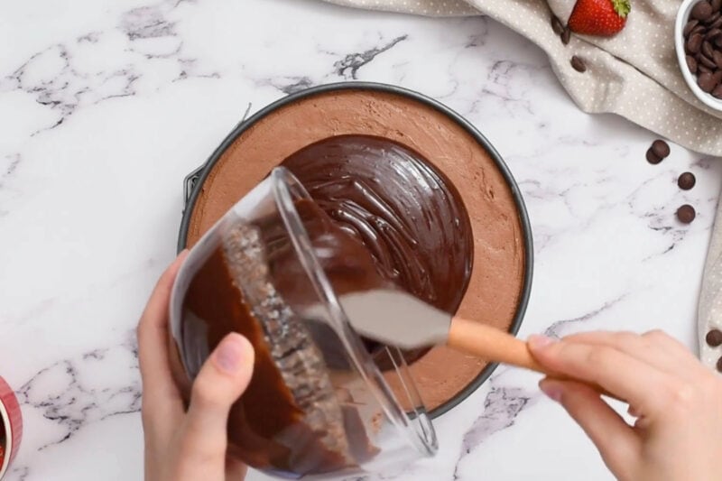 pouring chocolate ganache over chocolate mousse cake in a springform pan.