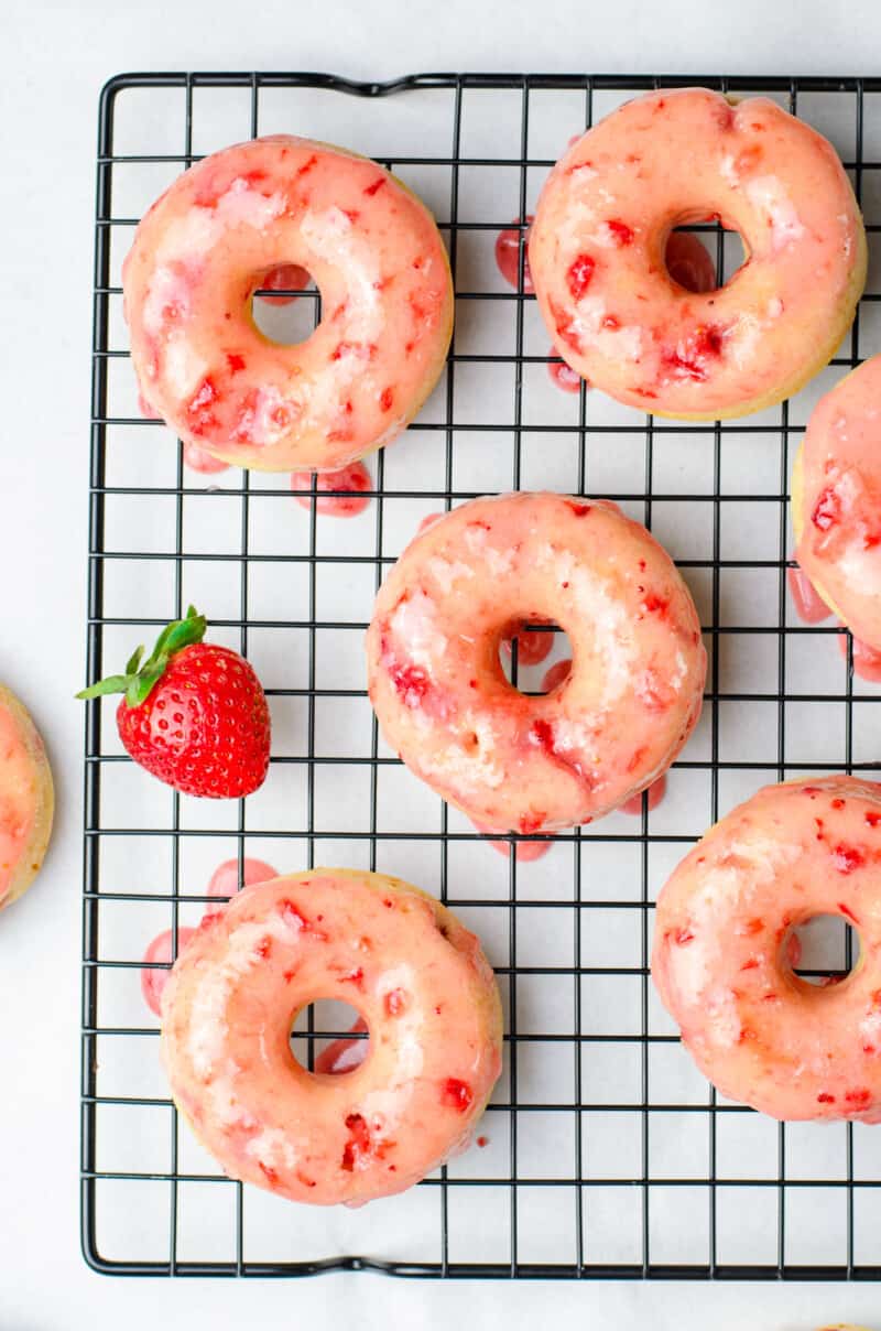 overhead image of baked strawberry donuts with strawberry glaze on a cooling rack