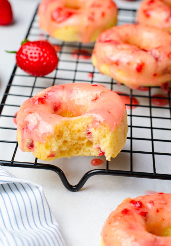 bite taken from a strawberry donut on a cooling rack