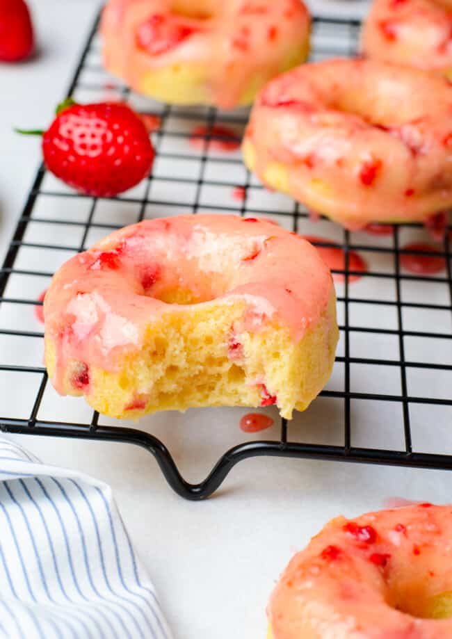 bite taken from a strawberry donut on a cooling rack
