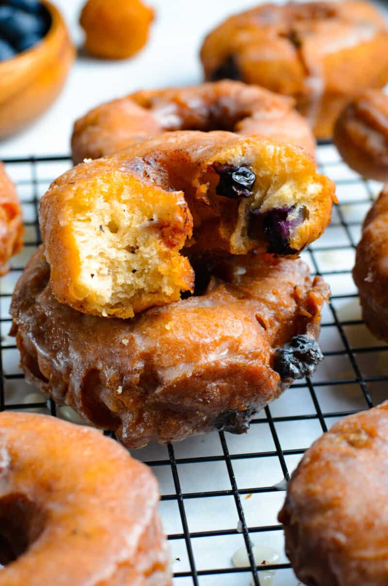 stack of 2 blueberry donuts on a cooling rack with a couple bites taken from the top donut