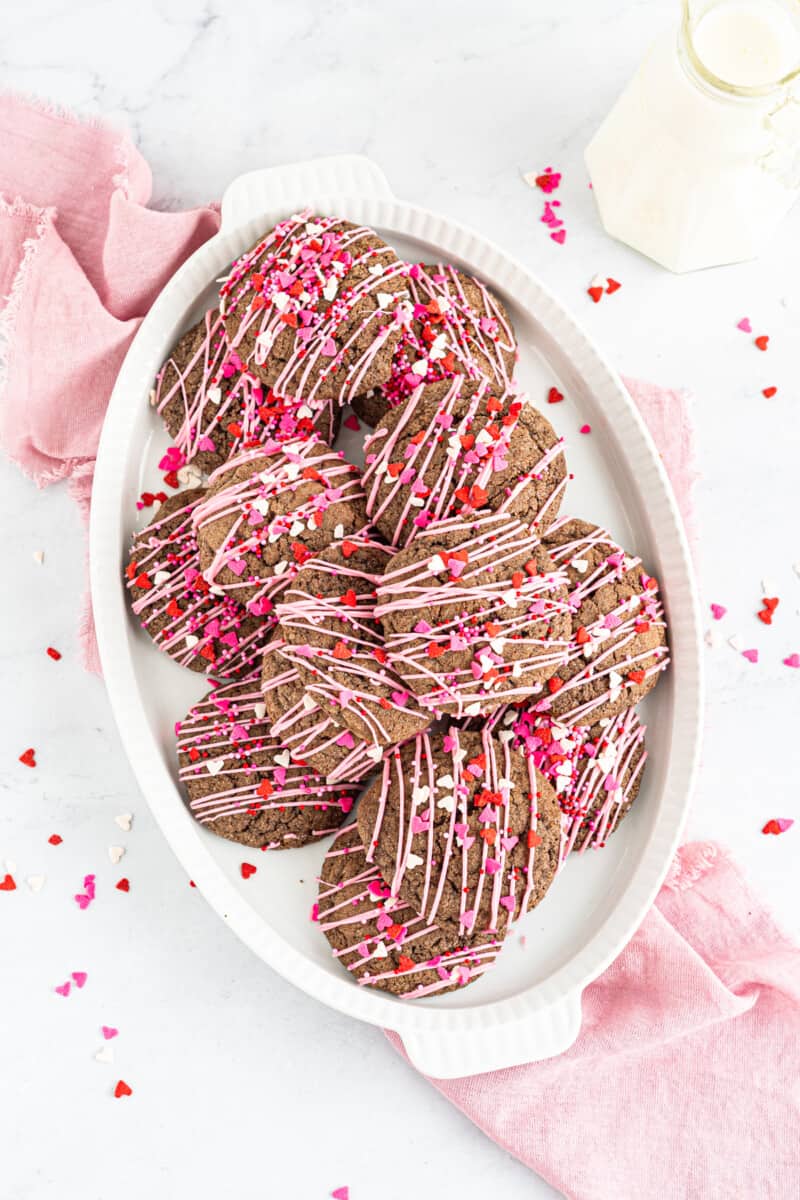 overhead image of chocolate sugar cookies decorated with a drizzle of pink icing and Valentine's Day sprinkles on a white plate