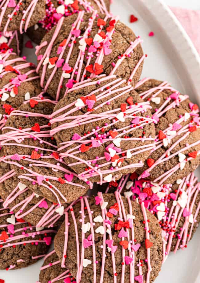 chocolate sugar cookies decorated with a drizzle of pink icing and Valentine's Day sprinkles on a white plate