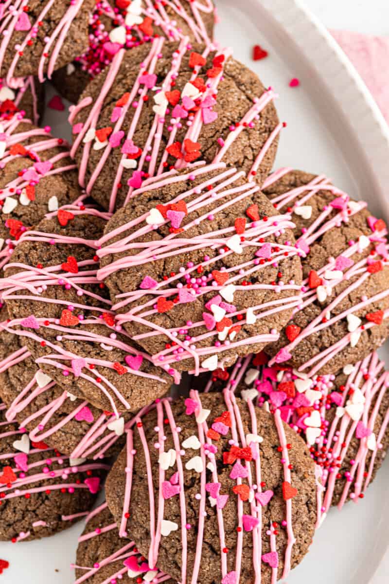 chocolate sugar cookies decorated with a drizzle of pink icing and Valentine's Day sprinkles on a white plate