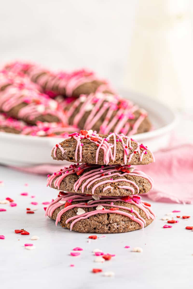 stack of 3 chocolate sugar cookies decorated with a drizzle of pink icing and Valentine's Day sprinkles