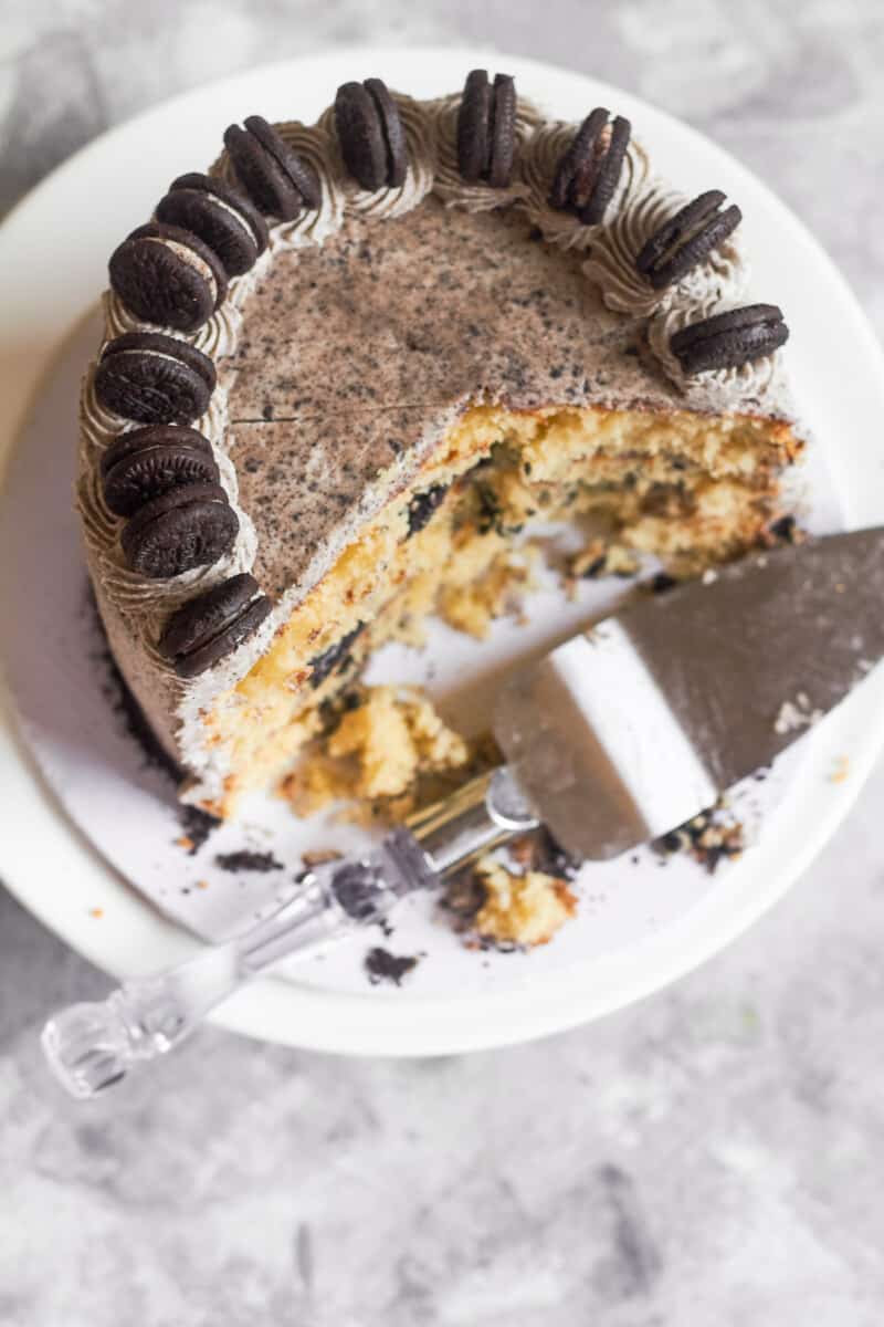 overhead image of cookies and cream cake on a cake stand with a few slices removed and a cake server