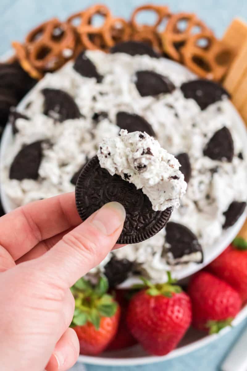 hand holding an Oreo cookie with cookies and cream dip on it