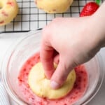 hand dipping a strawberry donut into strawberry glaze in a glass bowl