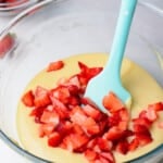 chopped strawberries added to donut batter in a glass bowl with a spatula
