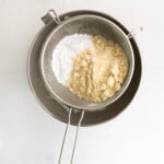 granulated sugar and almond flour in a metal sieve over a metal bowl