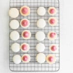 macaron pairs on a cooling rack with blood orange buttercream piped on half of the macaron shells