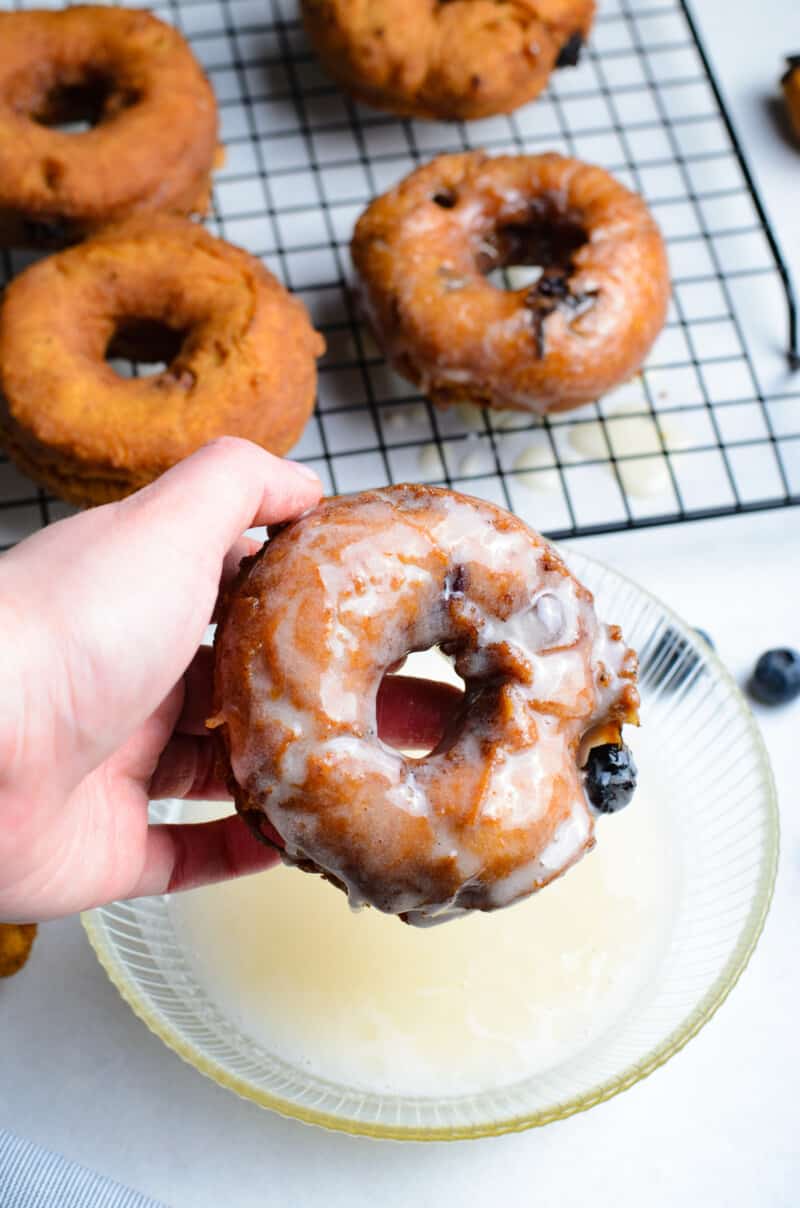 hand dipping a blueberry donut into glaze