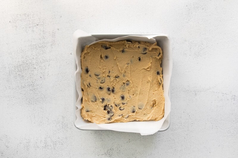 chocolate chip cookie bar dough spread into a baking pan before baking