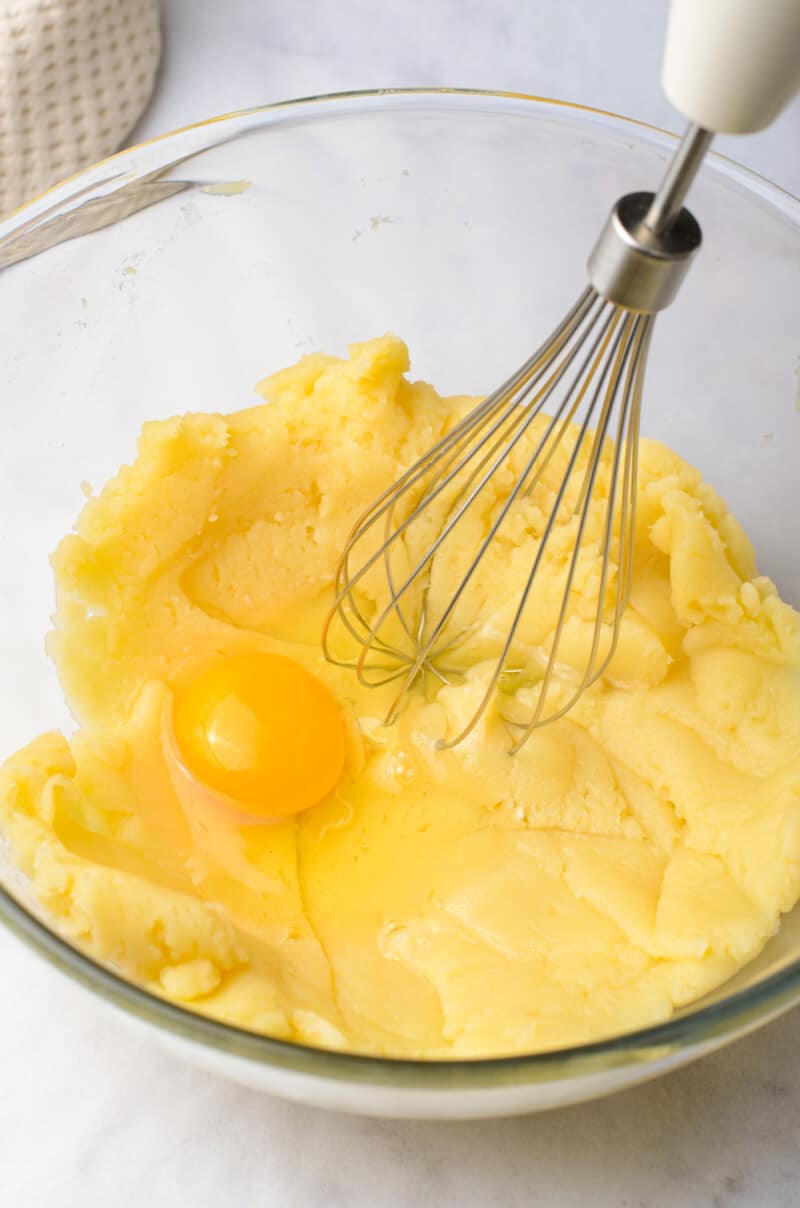 using a whisk to incorporate an egg into the dough in a glass bowl