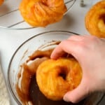 hand dipping a cruller into a bowl of chocolate glaze