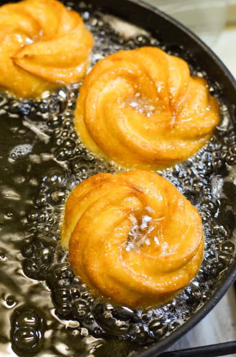 crullers frying in a pot of oil