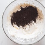 adding Oreo cookie crumbs to buttercream in a glass bowl