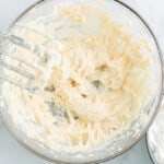 creamed cream cheese and powdered sugar in a glass bowl with a hand mixer
