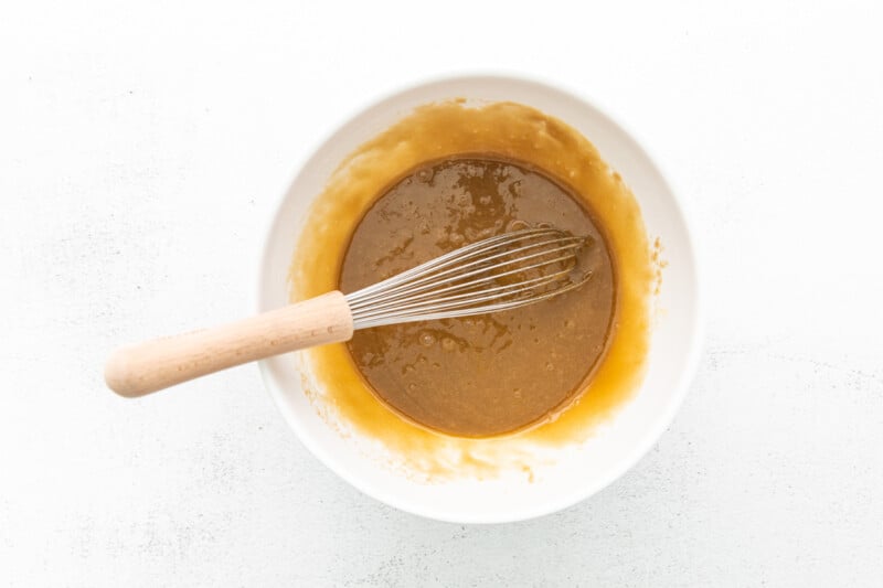 melted butter, brown sugar, egg, and vanilla in a white bowl with a whisk