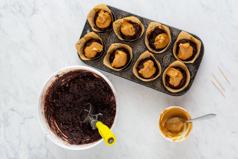 peanut butter spooned onto chocolate muffin batter in a muffin tin