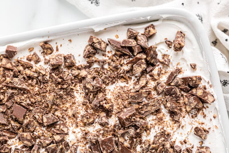 chopped toffee and cool whip spread onto the top of chocolate cake in a white baking dish