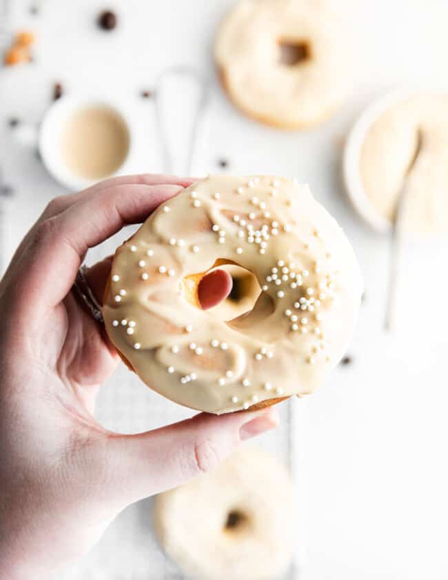hand holding a coffee donut with coffee icing and sprinkles on top