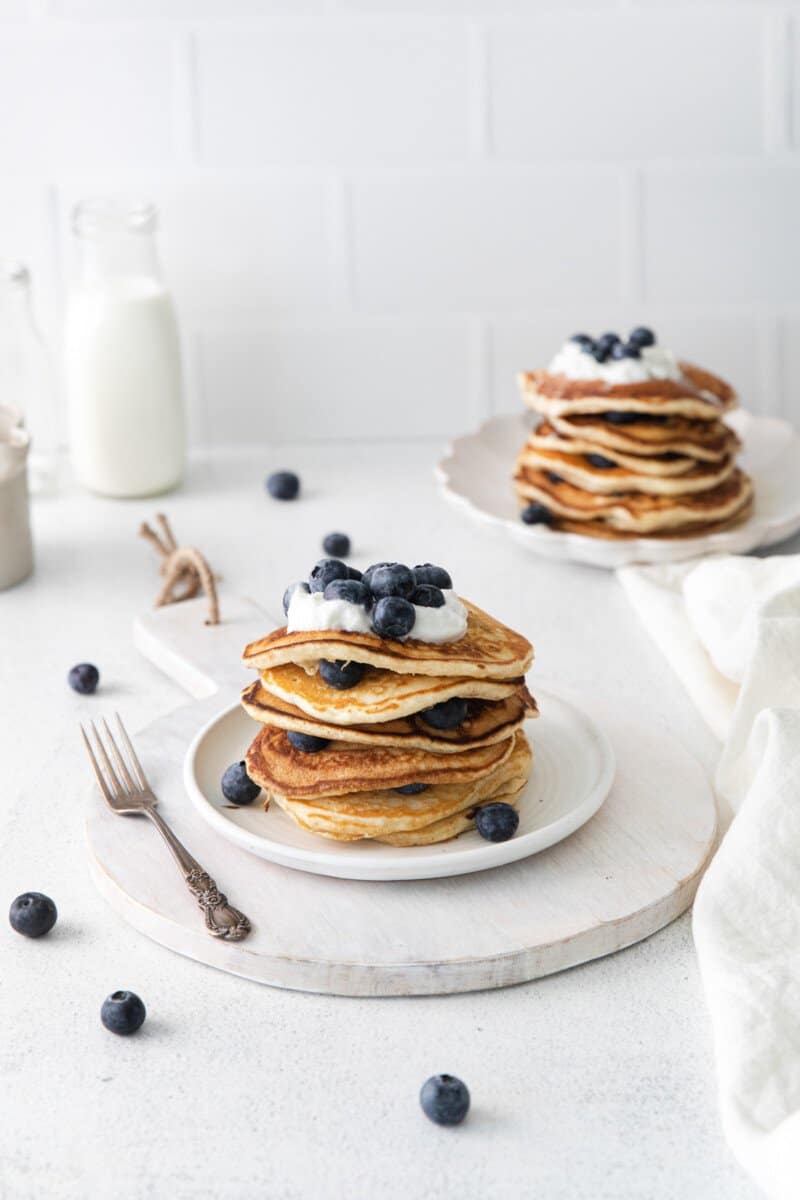2 white plates with stacks of blueberry pancakes